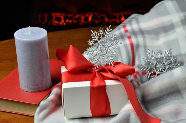 Foto scatola regalo con candela di libro rosso e fiocchi di neve decorativi davanti al camino