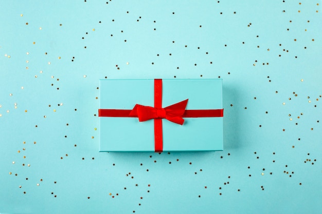 Gift box with red bow on a blue background. Holiday celebration concept. Top view, flat lay, copy space