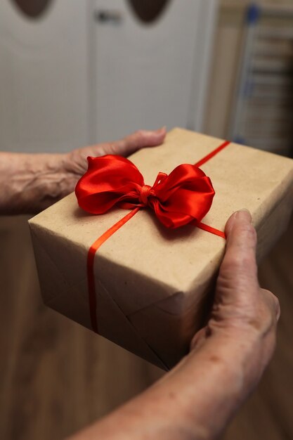 Gift box with red bow in grandmother hands macro