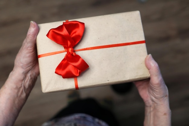 Gift box with red bow in grandmother hands macro