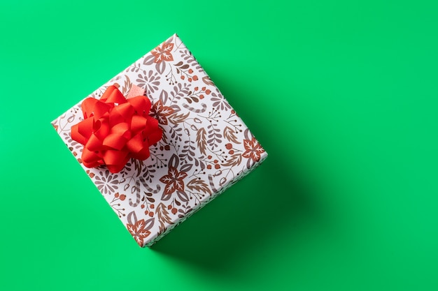 Подарочная коробка с красным бантом на зеленом фоне, на праздник. Копировать пространство
