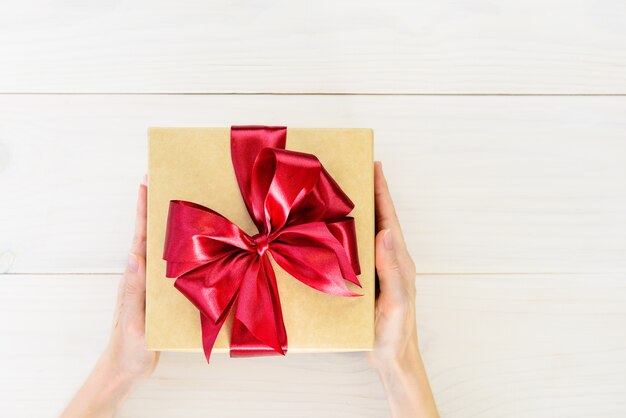 Gift in a box with a red bow in the hands of a man on a wooden background.