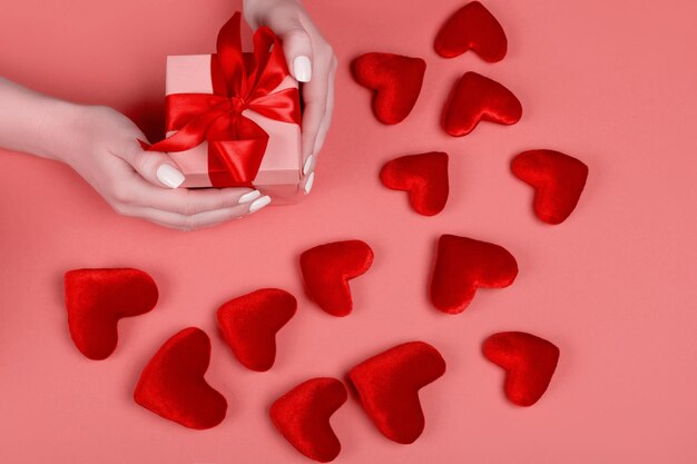 Gift box with red bow ribbon and glitter heart on living coral background for Valentines day