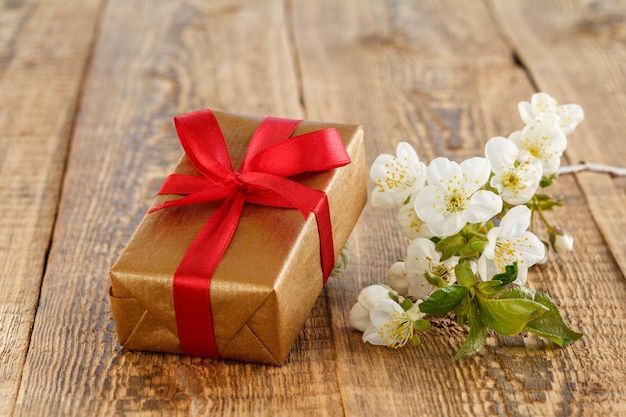 Gift box with red ribbons, branch of beautiful jasmine flowers on wooden boards. Concept of giving a gift on holidays.