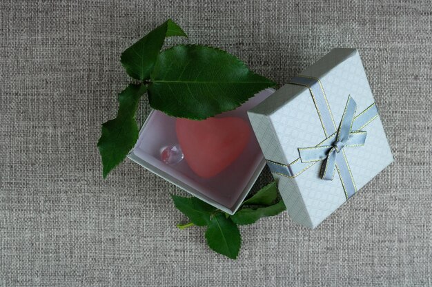 Gift box with rose leaves and heart and crystals inside close up on a gray background