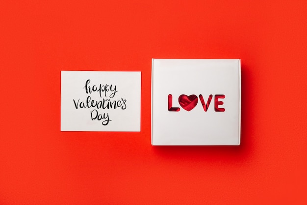 Gift box with text Love and card on a red background. Composition Valentine's Day. Banner. Flat lay, top view.