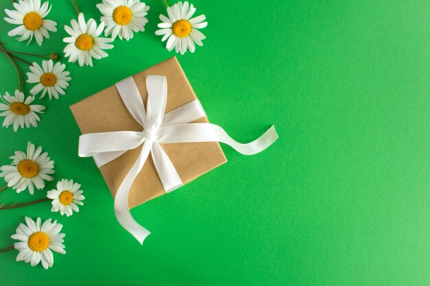 Gift box with white ribbon  and chamomile on the green background.Top view.