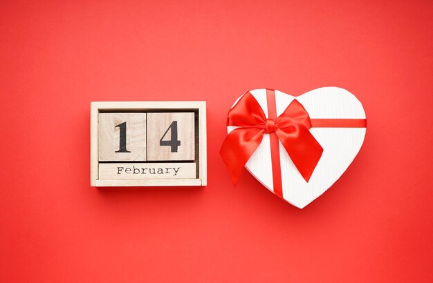 Gift box with a wooden calendar for Valentine's Day on a red background, top view.