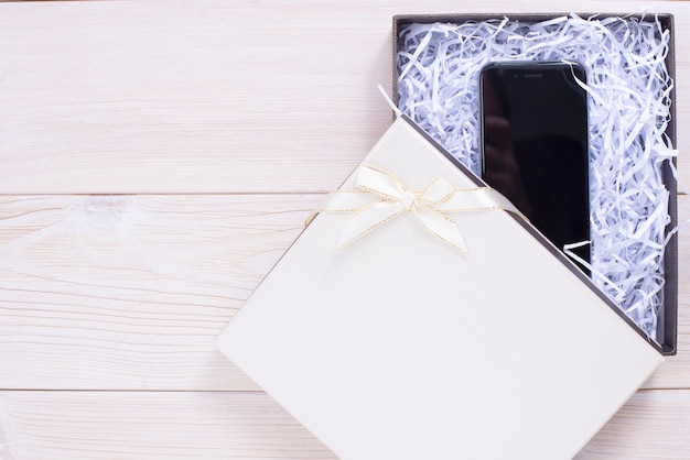 Gift box on wooden light background. Mobile phone