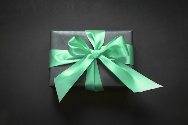 Gift box wrapped in black paper with neo mint ribbon on black surface.