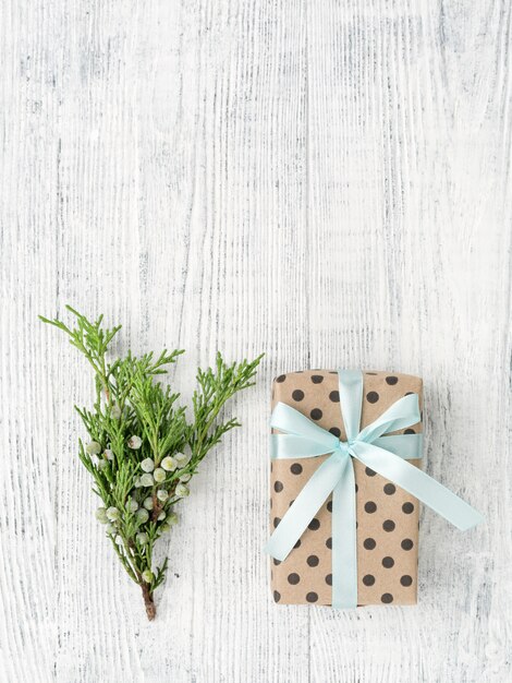 Gift box wrapped in brown paper and twig on white wooden table, copy space.