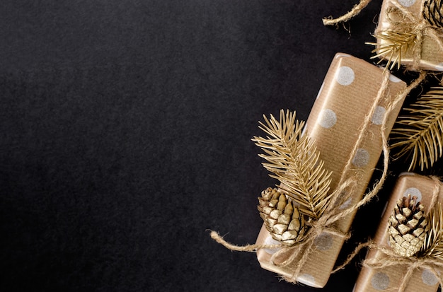 Gift box wrapped in craft paper with golden cone and fir on black background. 