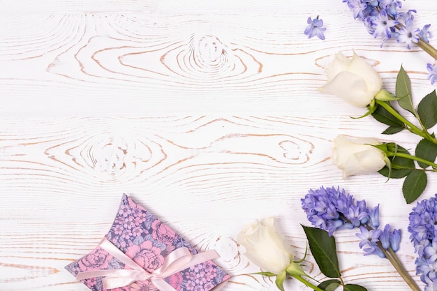 Una confezione regalo avvolta in carta e fiori blu, rose bianche su un tavolo bianco