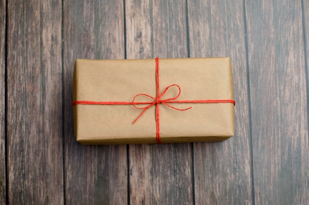 Gift box wrapped in recycled paper with red twine on wood.