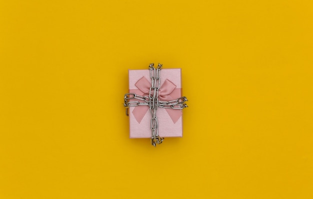 Gift box wrapped in a steel chain on a yellow background. Top view