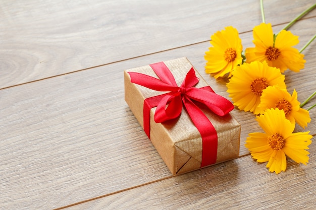 Gift box wrapped with red ribbon on wooden boards decorated with yellow flowers. Top view with copy space.