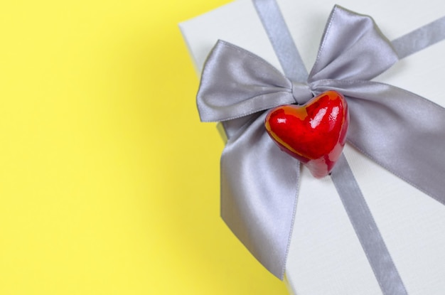 Gift box on a yellow background closeup Red heart on a gift box copy space