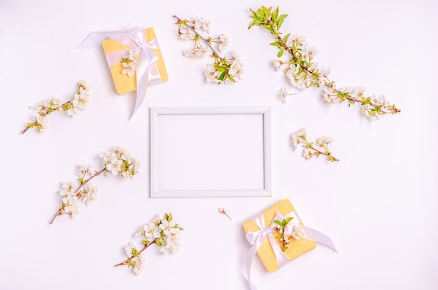 Gift boxes, blossoming cherry branches with a frame for text on a white background with copy space. Flat lay, 8 March, Mother's Day, banner. Top view