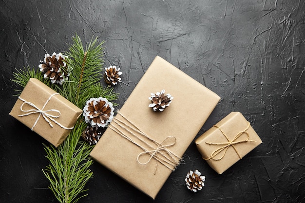 Gift boxes and green Christmas tree branch with pine cone on dark background top view