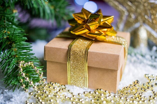 Gift boxes packing with a bow and ribbon of gold color and decorations with ornament balls on the snow on a bokeh background for the new year