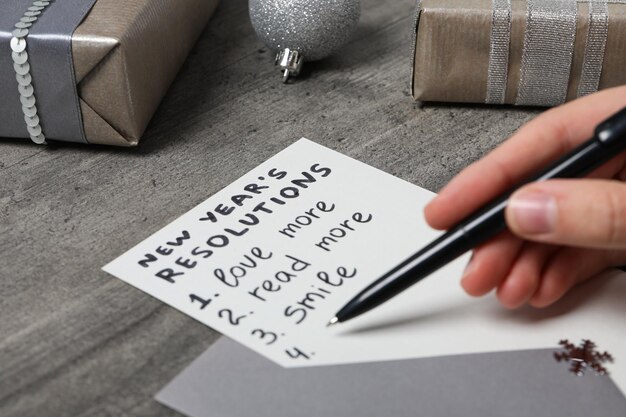 Photo gift boxes paper with list and pen in hand on gray wooden background close up