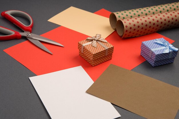 Подарочные коробки в горошек, упаковочная бумага, цветная бумага и ножницы на сером фоне