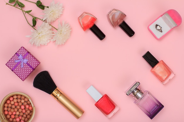 ピンクの背景にギフトボックス、パウダー、マニキュア、香水瓶、ブラシ、花。女性の化粧品とアクセサリー。上面図。