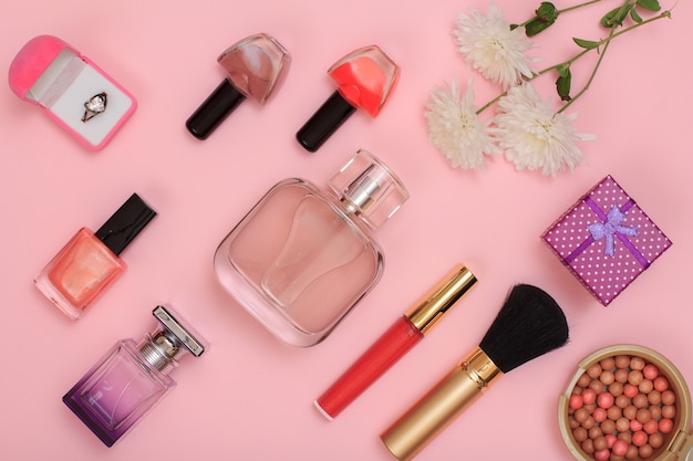 Gift boxes, powder, nail polish, bottles of perfume, lipstick, brush and flowers on a pink background. Women cosmetics and accessories. Top view.