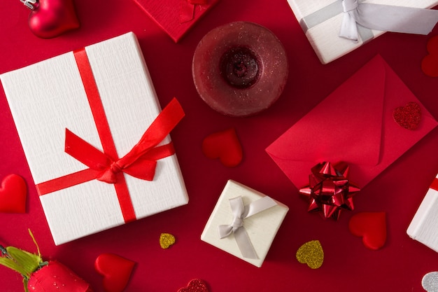 Gift boxes, red paper envelope and red hearts on red background