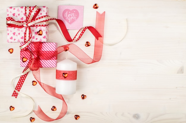 Gift boxes with candle, greeting card, hearts and ribbon on wood background