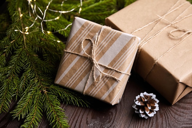 Gift boxes with Christmas light and tree branch with cone on brown wooden background