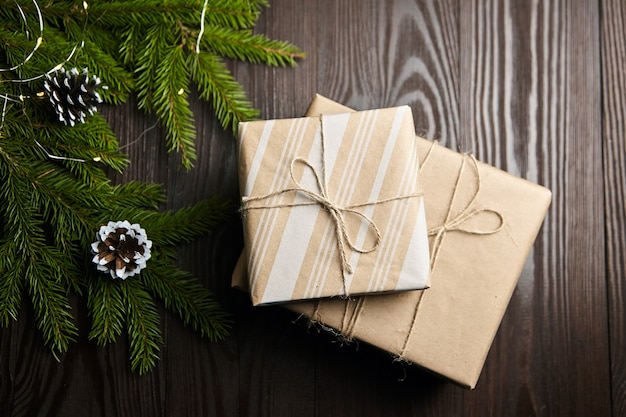 Gift boxes with Christmas light and tree branch with cones on brown wooden background