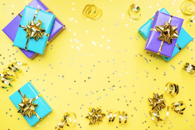 Gift boxes with gold ribbons and bows, confetti stars on a yellow background. Copy space Flat lay. Greeting card for birthday party, Christmas Wedding mother's Day.