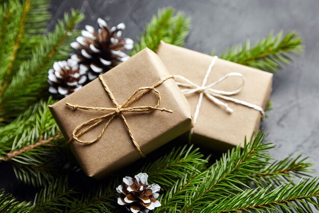 Gift boxes with green Christmas tree branches and cones on dark background