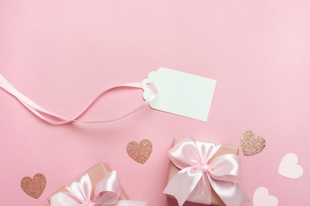 gift boxes with pink ribbon and hearts on pastel pink background.