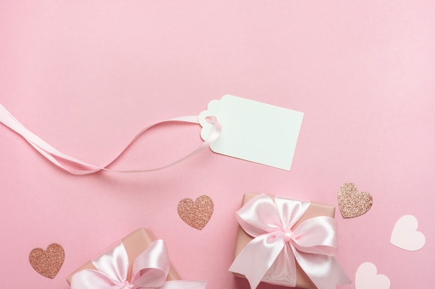 Gift boxes with pink ribbon and hearts on pastel pink background.