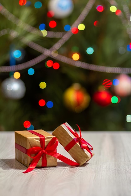 Gift boxes with red bows and blurred christmas tree with\
twinkling party lights and toy balls