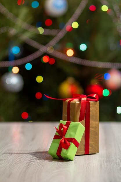 Gift boxes with red bows and blurred Christmas tree with twinkling party lights and toy balls