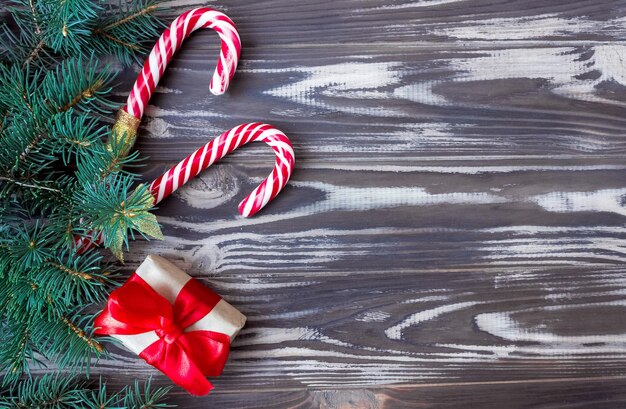 나무 배경에 빨간 리본, 카라멜 스틱, 전나무 가지가 있는 선물 상자. 공간을 복사합니다. 크리스마스와 새 해 개념입니다. 엽서. 단조롭게