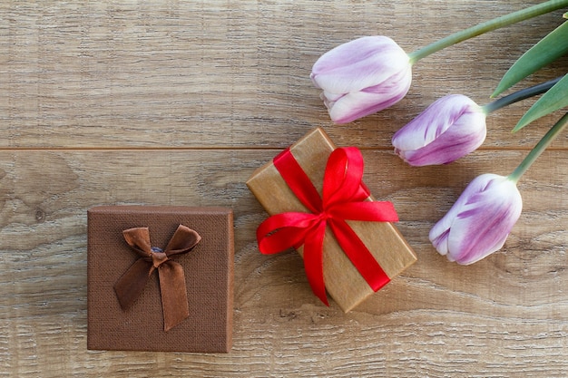 Gift boxes with ribbons and beautiful lilac tulips on the wooden boards Top view