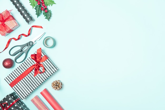 Gift boxes wrapped in black and white striped and red paper with wrapping materials over a blue background. Christmas presents preparation. 