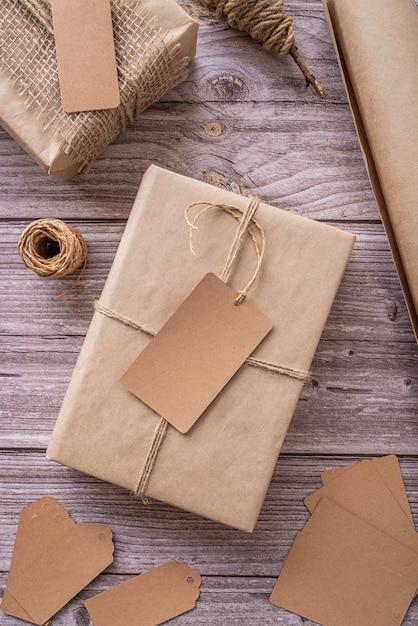 Gift boxes wrapped in craft paper with tags and labels on wooden  top view flat lay