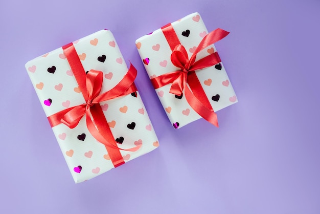 Gift boxes wrapped in heart pattern paper with red ribbon bow on pink background