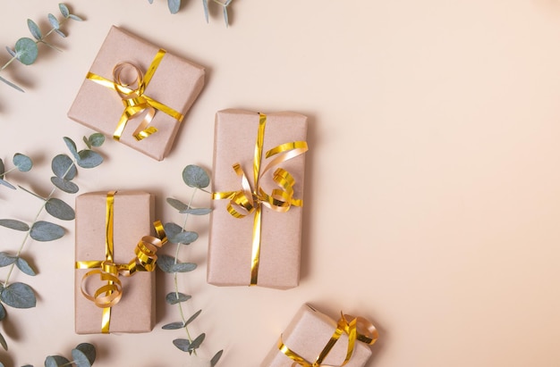 Gift boxes wrapped in kraft paper with golden ribbon and eucalyptus on pastel beige background Holiday present concept Top view