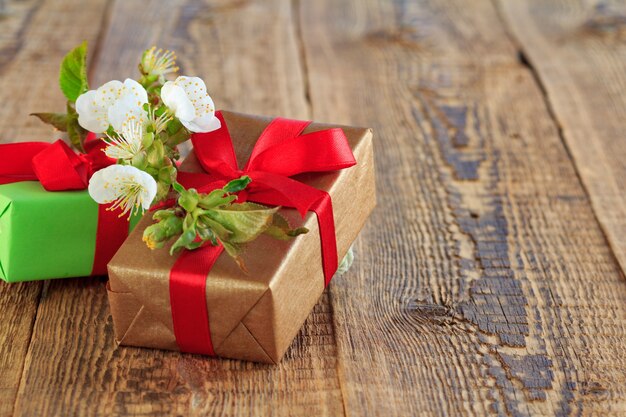 Подарочные коробки, обернутые красными лентами, украшенные цветами жасмина на деревянных досках.