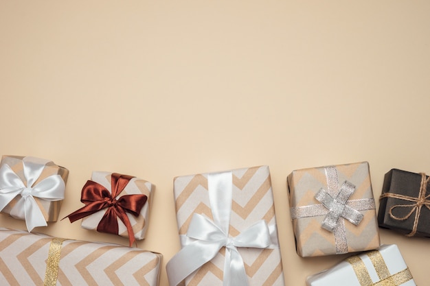 gift boxes wrapped with white, silver and golden ribbon and bow on beige table.