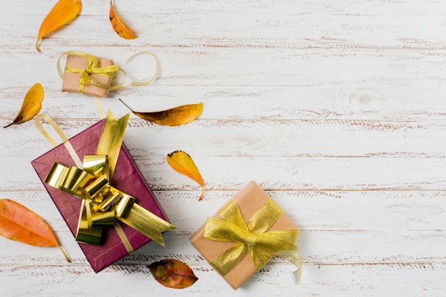 Photo gift boxes in wrapping paper with ribbons and autumn leaves on a white wooden background