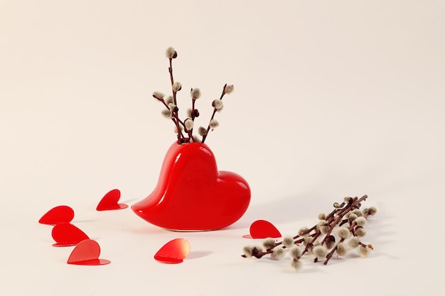 Gift card red heartshaped vase with a bouquet of willow branches scattered red paper hearts nearby white background space for text