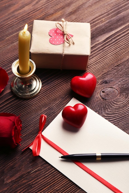 ボックスの赤いバラのペンと木製の背景にキャンドルとバレンタインデーのギフトカード
