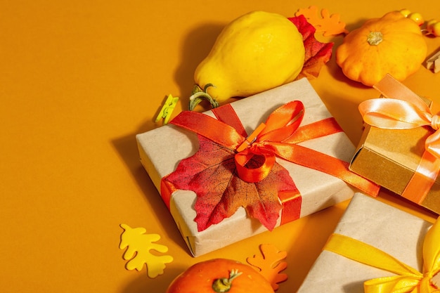 Gift concept in autumn colors. Wrapped boxes, festive fall decor, pumpkin, leaves, and berries. A trendy hard light, dark shadow, orange background, copy space